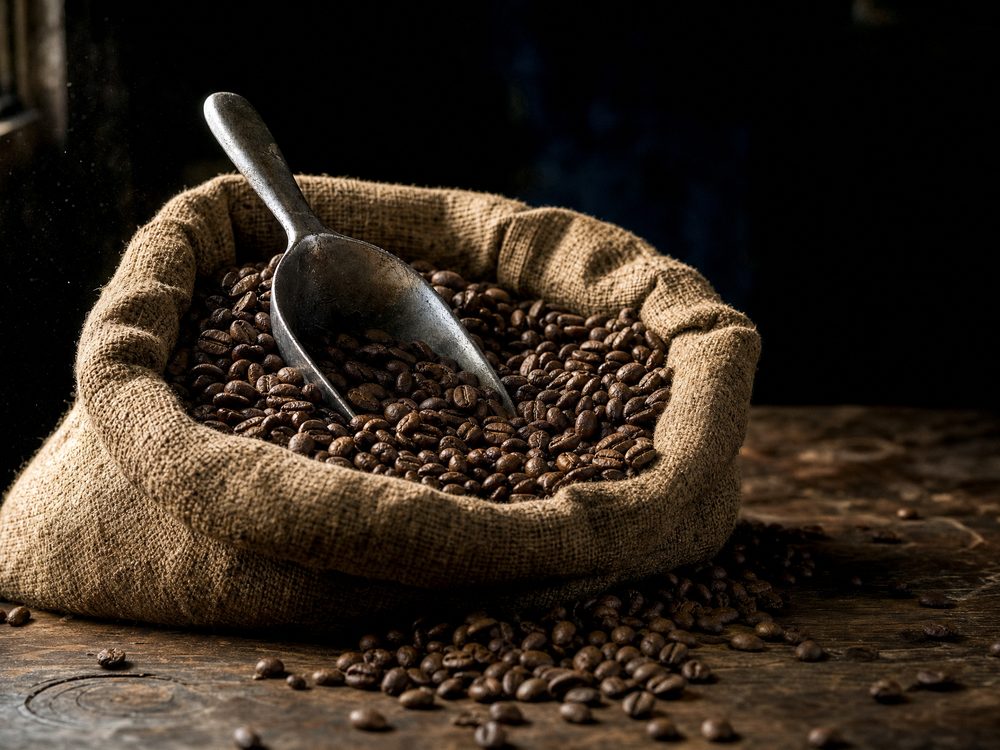 An open burlap sack of roasted coffee beans with a metal scoop resting in them